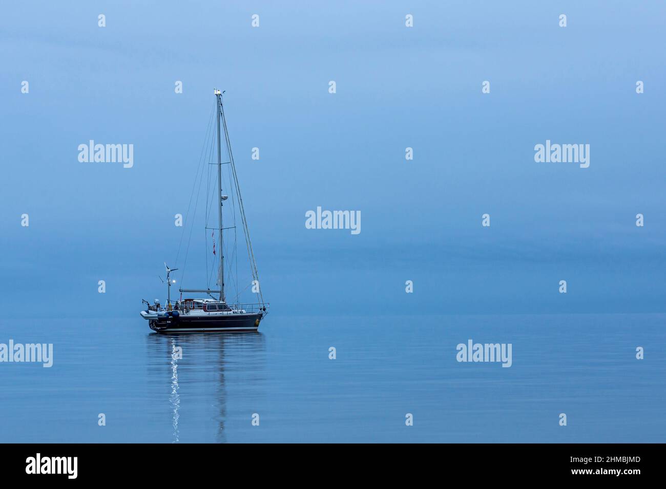 Das schwarze Segelboot ist allein und spiegelt sich während der blauen Stunde im ruhigen Meer wider, Dänemark, 30. August 2017 Stockfoto