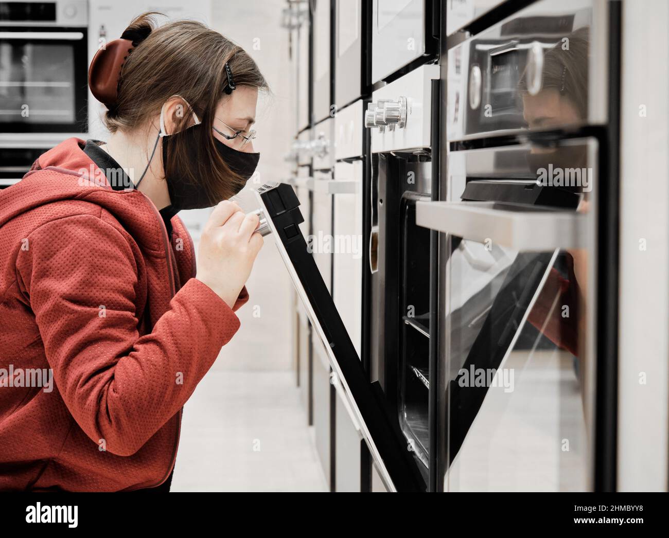 Frau in Maske gegen Virus in einem Geschäft wählt für kaufen einen Küchenofen Stockfoto