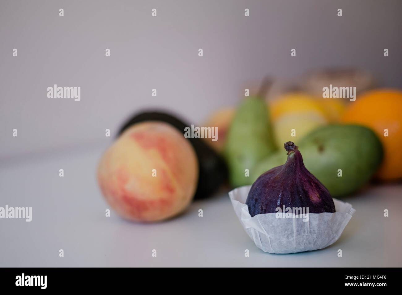Frische Feige im Vordergrund mit anderen Früchten auf hellem Hintergrund auf dem Tisch Stockfoto