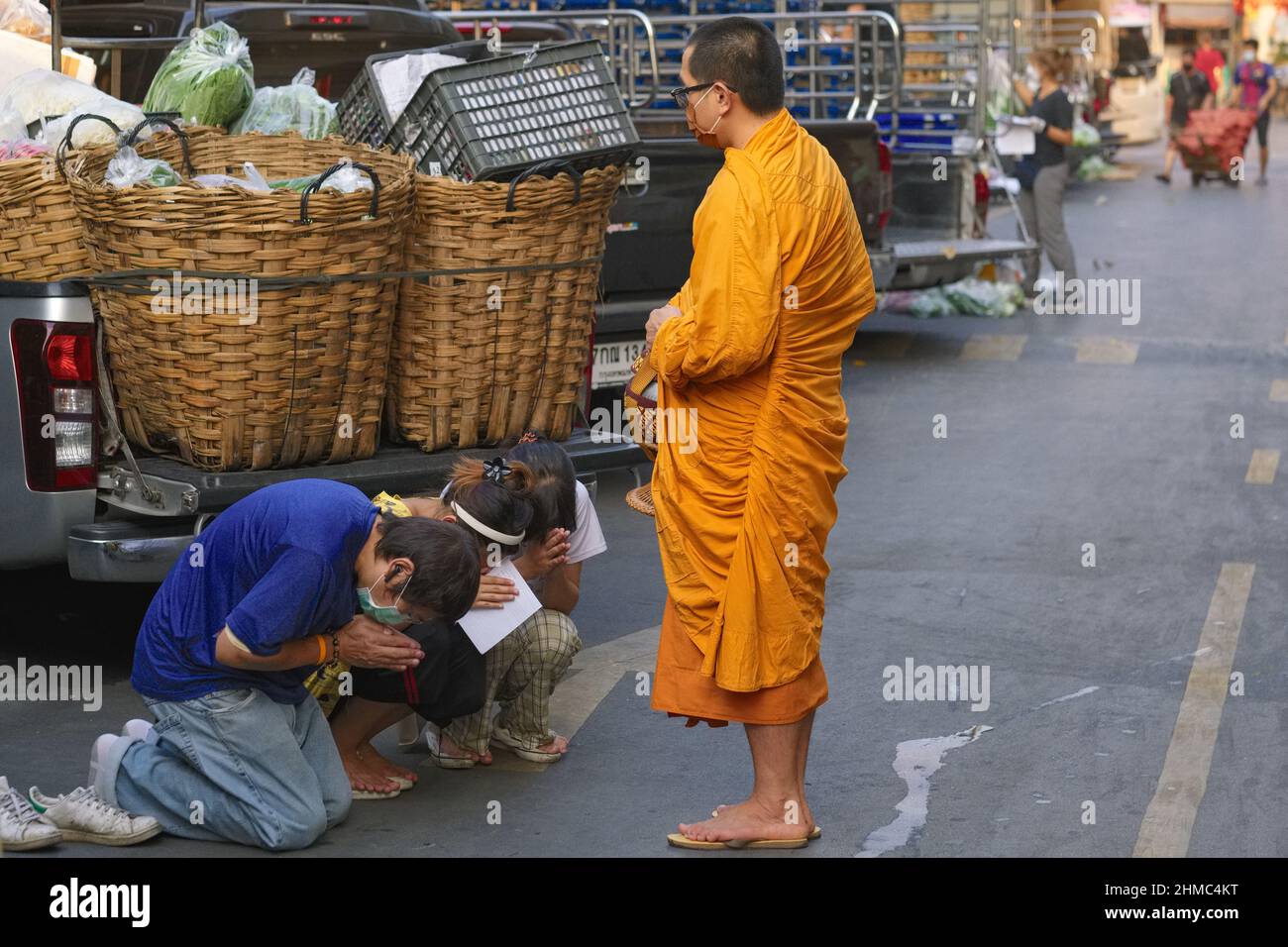 Drei junge Angestellte auf einem Markt in Bangkok, Thailand, knieten tief vor einem buddhistischen Mönch bei seiner morgendlichen Almosenrunde und baten um Segen Stockfoto