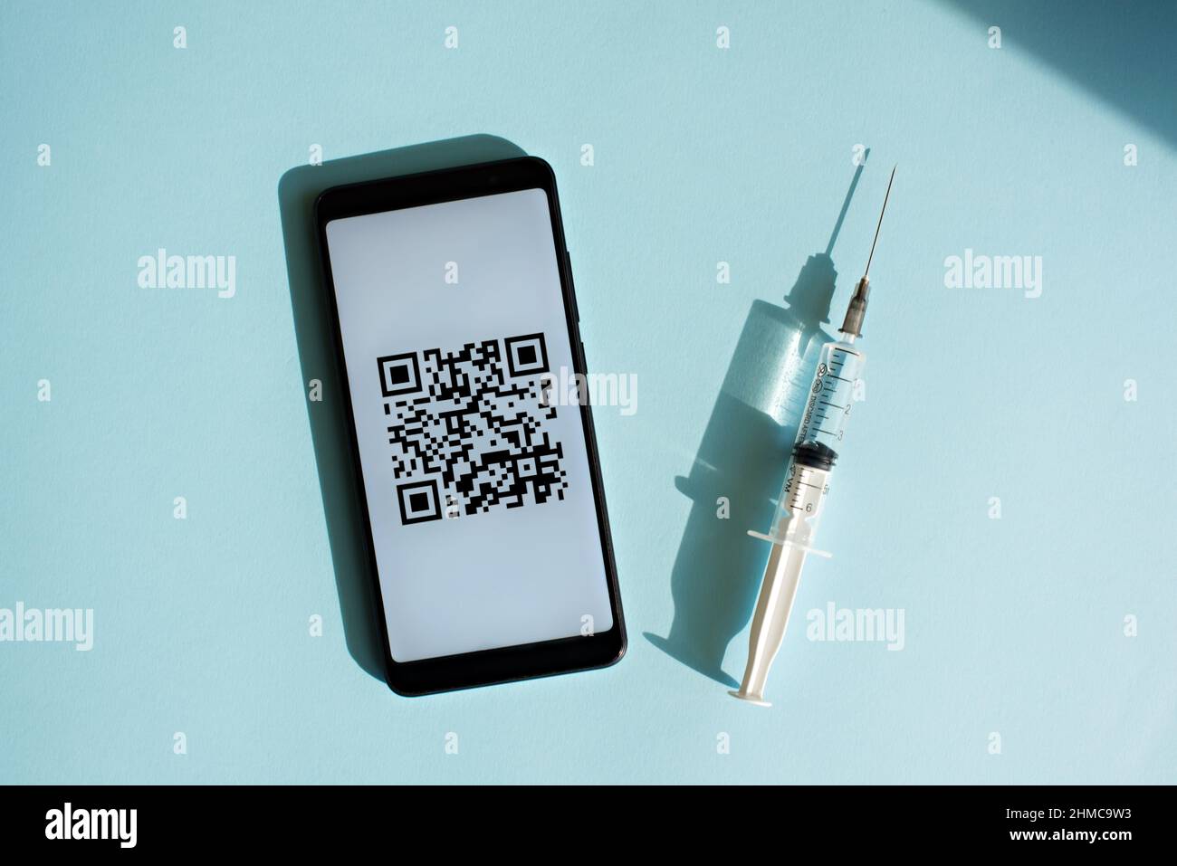 Smartphone mit Quar-Code des Impfzertifikats auf dem Bildschirm, Spritze und medizinischer Maske auf hellblauem Hintergrund. Stockfoto