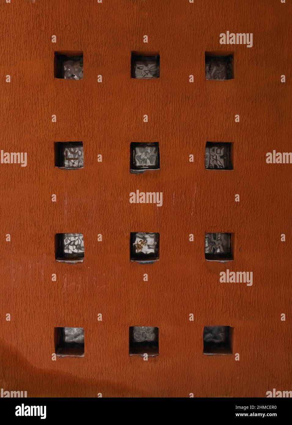 Orangefarbene Wand mit rustikaler Textur mit mehreren quadratischen Löchern Muster Stockfoto