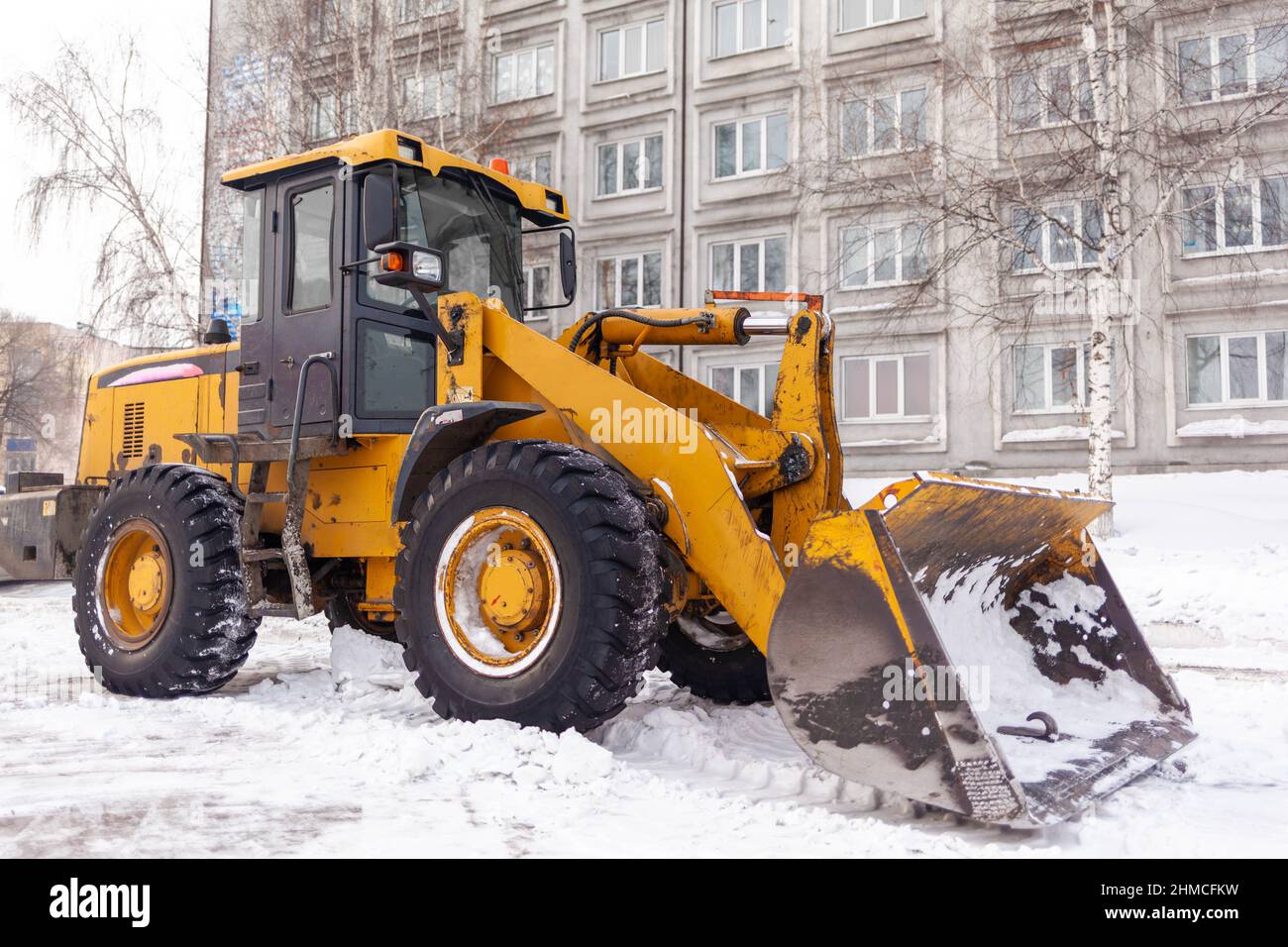 Großer orangefarbener Traktor reinigt Schnee von der Straße und lädt ihn in den LKW. Reinigung und Reinigung der Straßen in der Stadt vom Schnee im Winter. Schnee remo Stockfoto