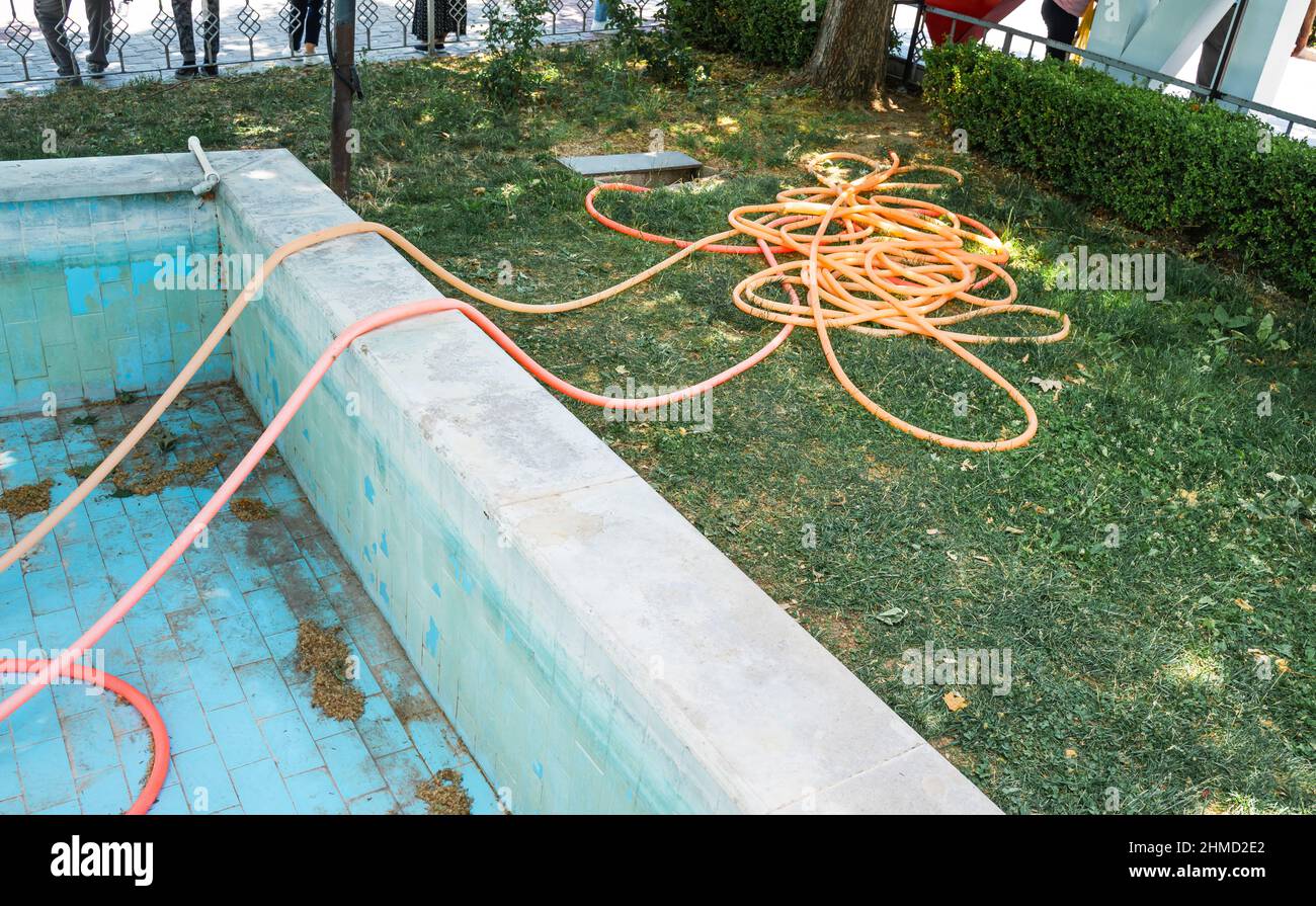 Schlauchbewässerung Ausrüstung auf grünem Gras in der Nähe eines leeren Schwimmbeckens. Stockfoto