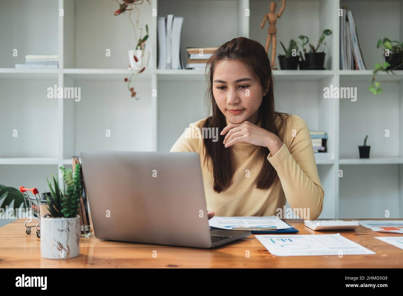 Attraktive asiatische Geschäftsfrau sitzt auf ihrem Arbeitsplatz im Büro. Junge Frau, die im Büro am Laptop arbeitet. Stockfoto