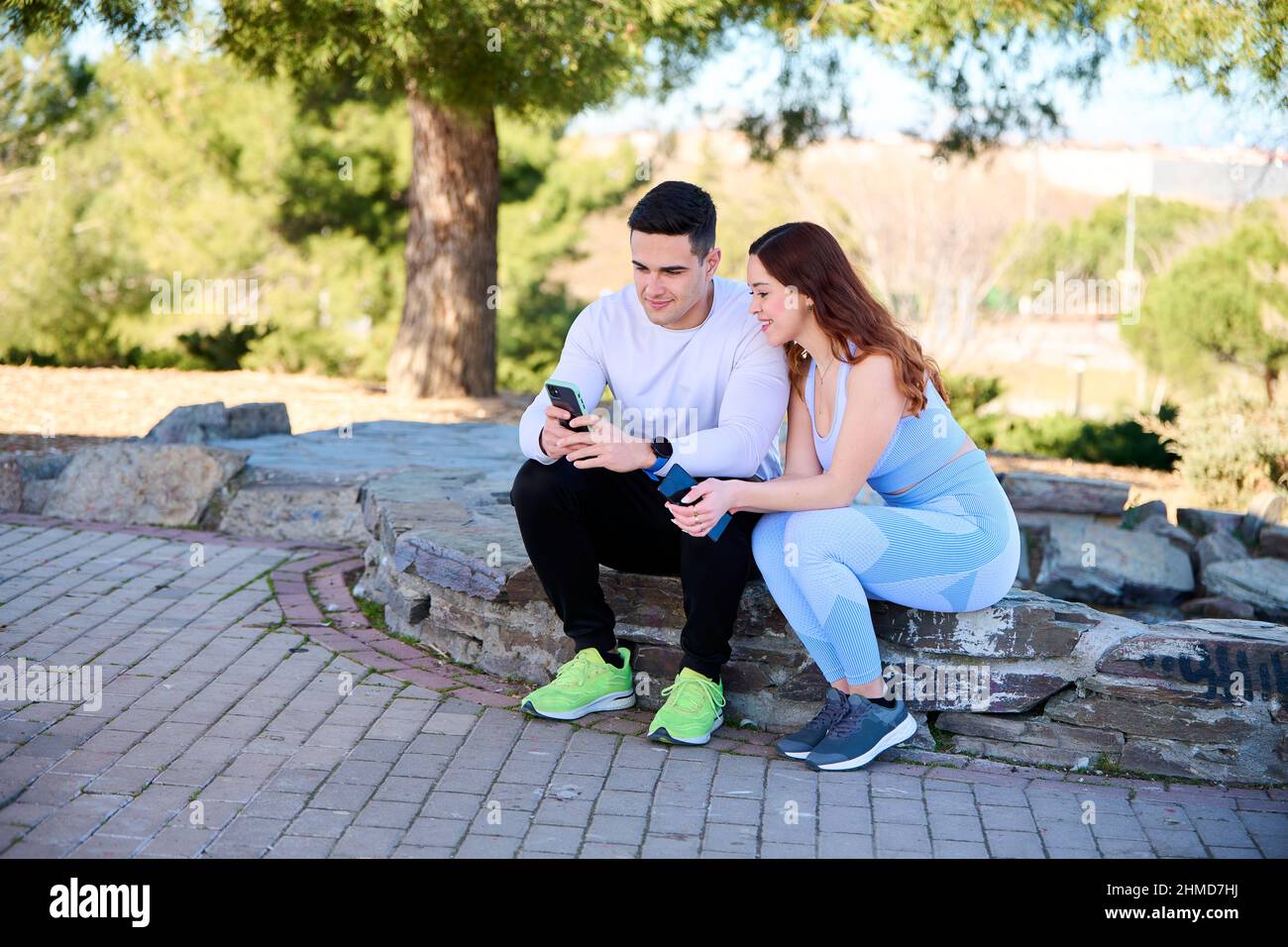 Junges Paar, das sich Online-Inhalte auf einem Smartphone in einem Park ansieht Stockfoto