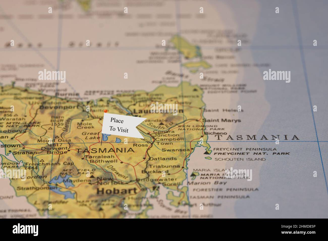 Eine Nahaufnahme einer kleinen Flagge mit dem Satz „Ort zu besuchen“ an einer Nadel, die in einer Illustration von Tasmanien Australien in einem Atlas angebracht wurde Stockfoto