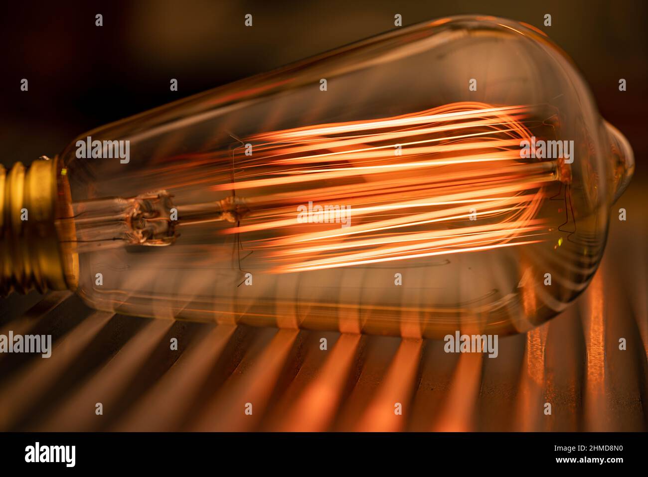 Eine helle, transparente Glühlampe aus Glas leuchtet mit einem schwachen, bernsteinfarbenen, feurigen Licht, das auf einer glatten Wellmetalloberfläche in der Werkstatt eines Ingenieurs liegt Stockfoto