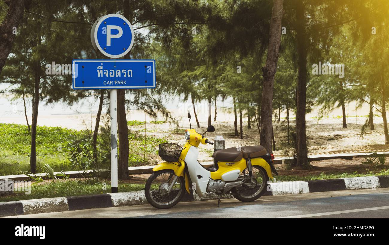 Ein leuchtend gelbes Honda Motorrad, Super Cub, steht neben einem Verkehrsschild, das als Parkplatz gekennzeichnet ist. Tang Book auf Thai bedeutet Parken. Auf 10.09.2 Stockfoto