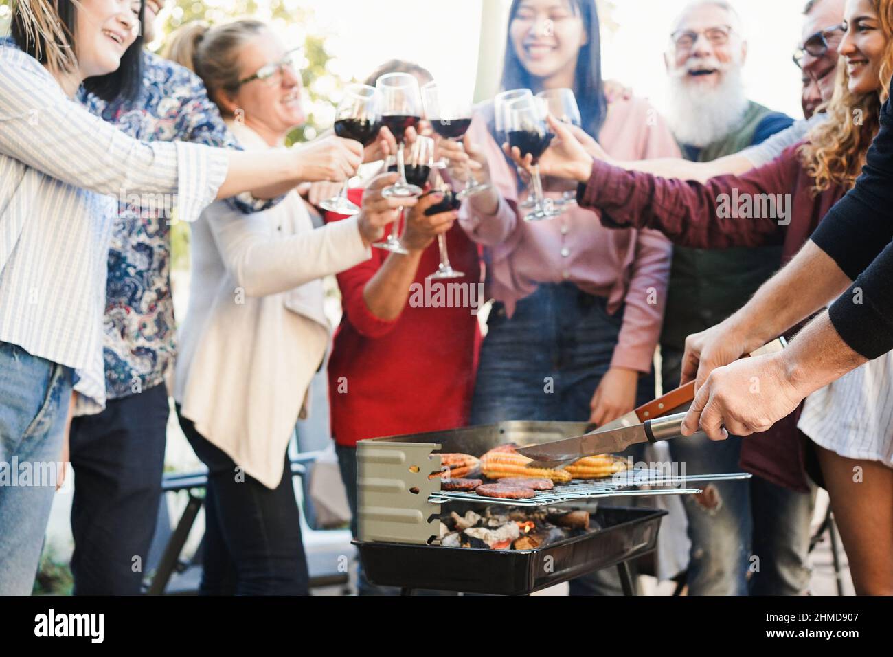 Generationsübergreifende Menschen, die beim Barbecue-Abendessen im Freien Spaß mit Wein haben - konzentrieren Sie sich auf die rechte Hand Stockfoto