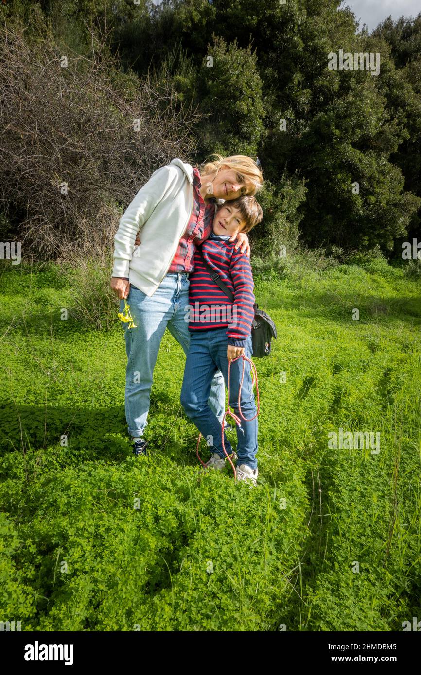 Lächelnde Mutter und Sohn mit den Armen auf grünen Büschen auf dem Feld stehend Stockfoto