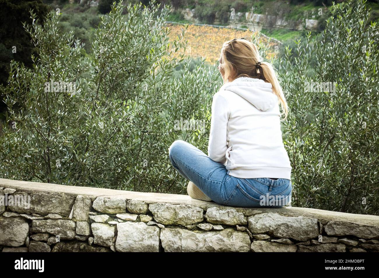 Frau, die auf der umgebenden Wand neben grünen Pflanzen sitzt Stockfoto