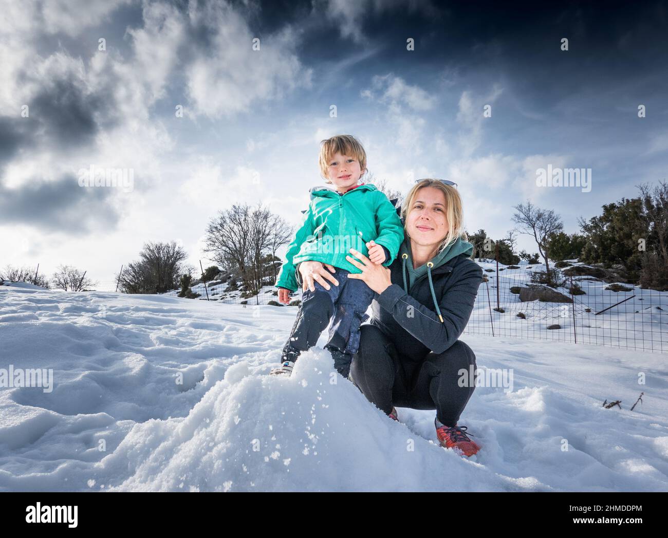 Glückliche Mutter hält kleinen Jungen in schneebedeckten Feld gegen bewölkten Himmel Stockfoto