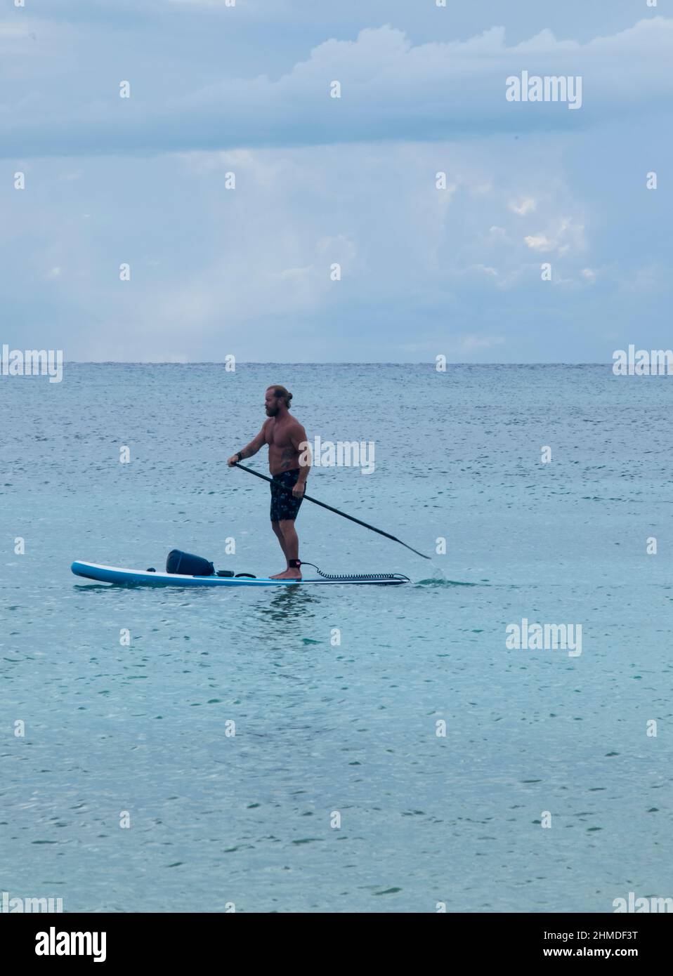 Ein sportlicher junger Mann schwebt mit einem Paddel in der Hand am Strand in Playa del Carmen, Mexiko Stockfoto