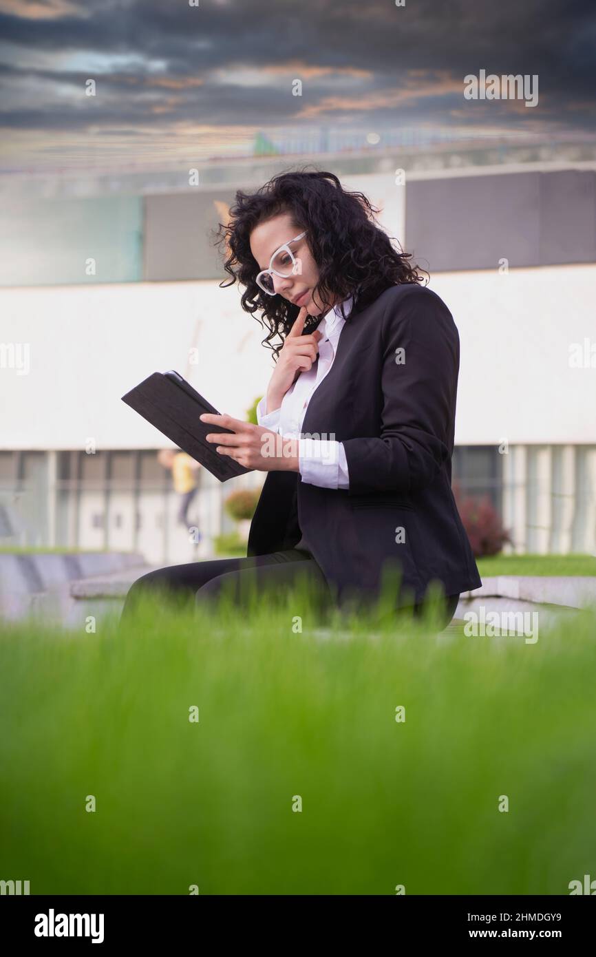 Frau im Anzug, die auf ihrem Tablet nachdenkt und Online-Nachrichten liest Stockfoto