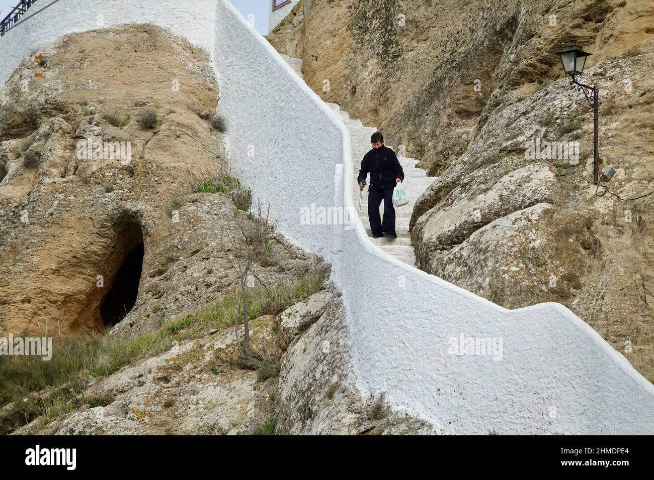 Iznájar, Córdoba-Spanien; 23. Januar 2022: Ältere Menschen mit Gehstock, die eine Treppe aus weißem Stein mit Schwierigkeiten hinuntergehen Stockfoto