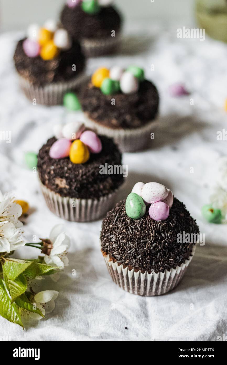 Hausgemachte Oster-Schokolade-Cupcakes mit Schokoladenbutter-Creme-Zuckerguss und Süßigkeiten-Eiern. Osterbrunch. Frühlingsblumen-Dekoration. Auf weißem Leinentisch Stockfoto