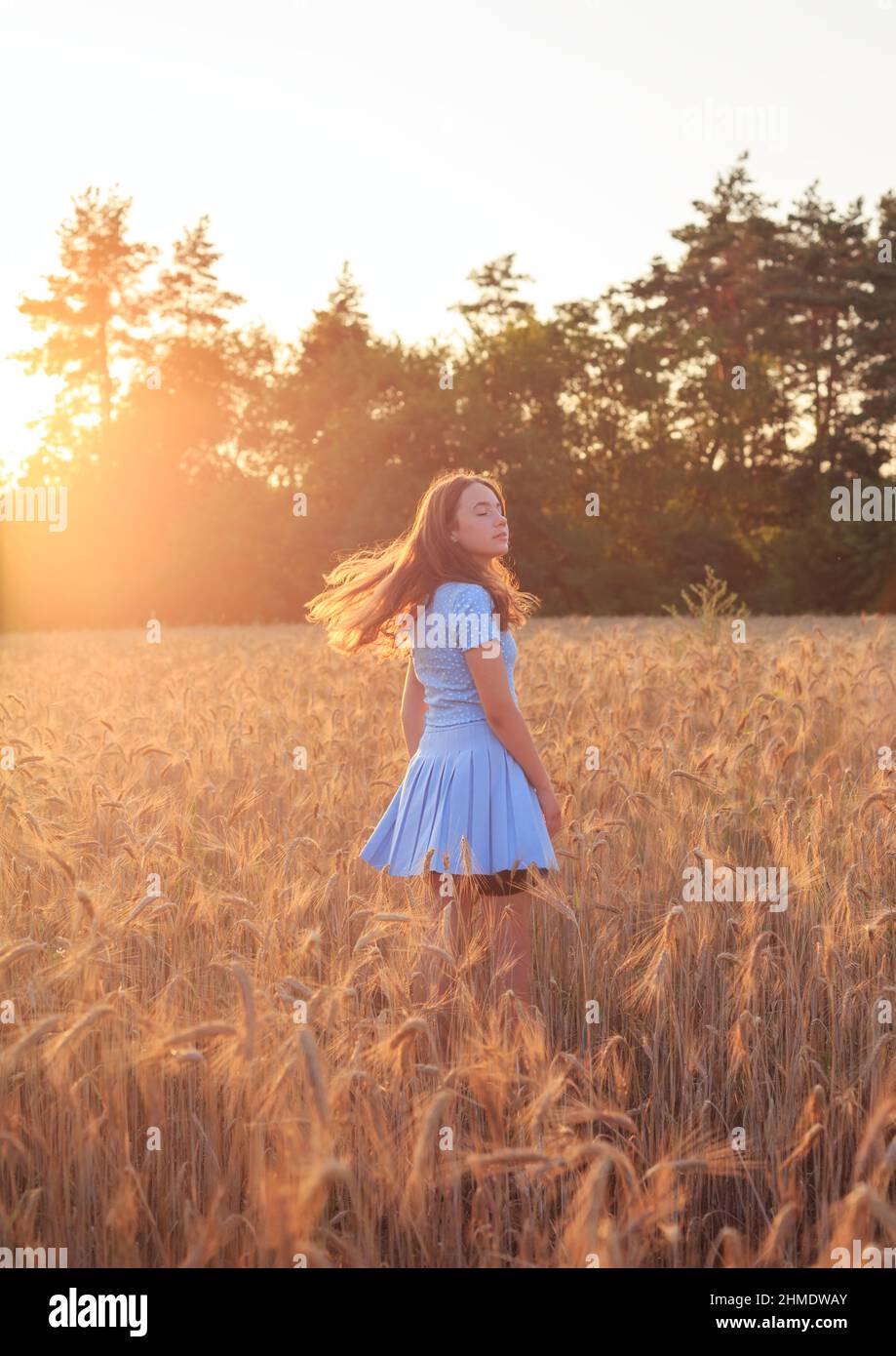 Happy teen girl lächelt auf Weizenfeld und berührt Ähren von Weizen mit der Hand. Schöner Teenager, der die Natur bei warmem Sonnenschein in einem Weizenfeld genießt Stockfoto