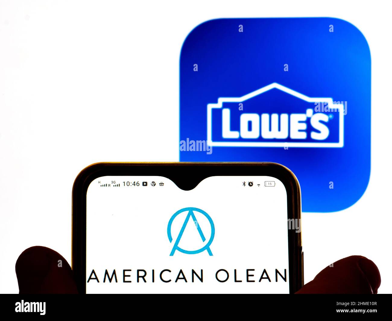 In dieser Abbildung wird das American Olean-Logo auf einem Smartphone-Bildschirm und im Hintergrund ein Logo von Lowe's Companies, Inc. Angezeigt Stockfoto