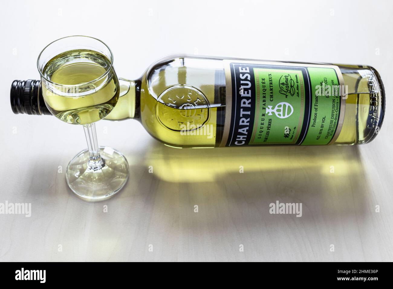 Moskau, Russland - 3. Februar 2022: Likörglas und eine liegende Flasche grünen Chartreuse-Likörs auf einem hellen Tisch (Schwerpunkt Weinglas). Der Likör war Stockfoto