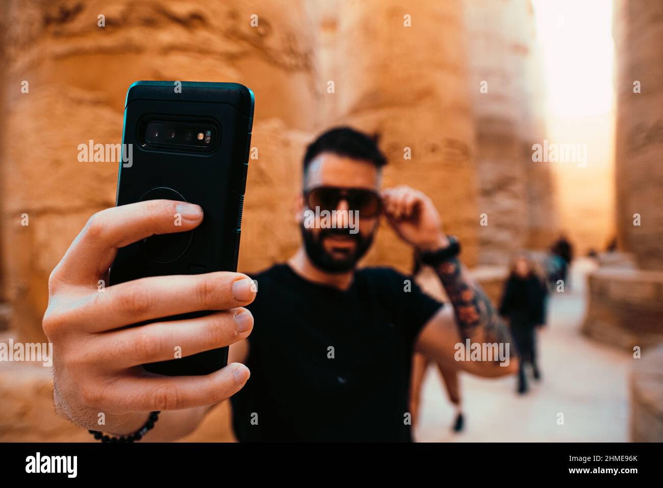 Hispanic Mann trägt eine Sonnenbrille und nimmt ein Selfie in luxor, umgeben von alten ägyptischen Säulen. Konzentrieren Sie sich auf das Smartphone, Reisende, die Fotos machen Stockfoto