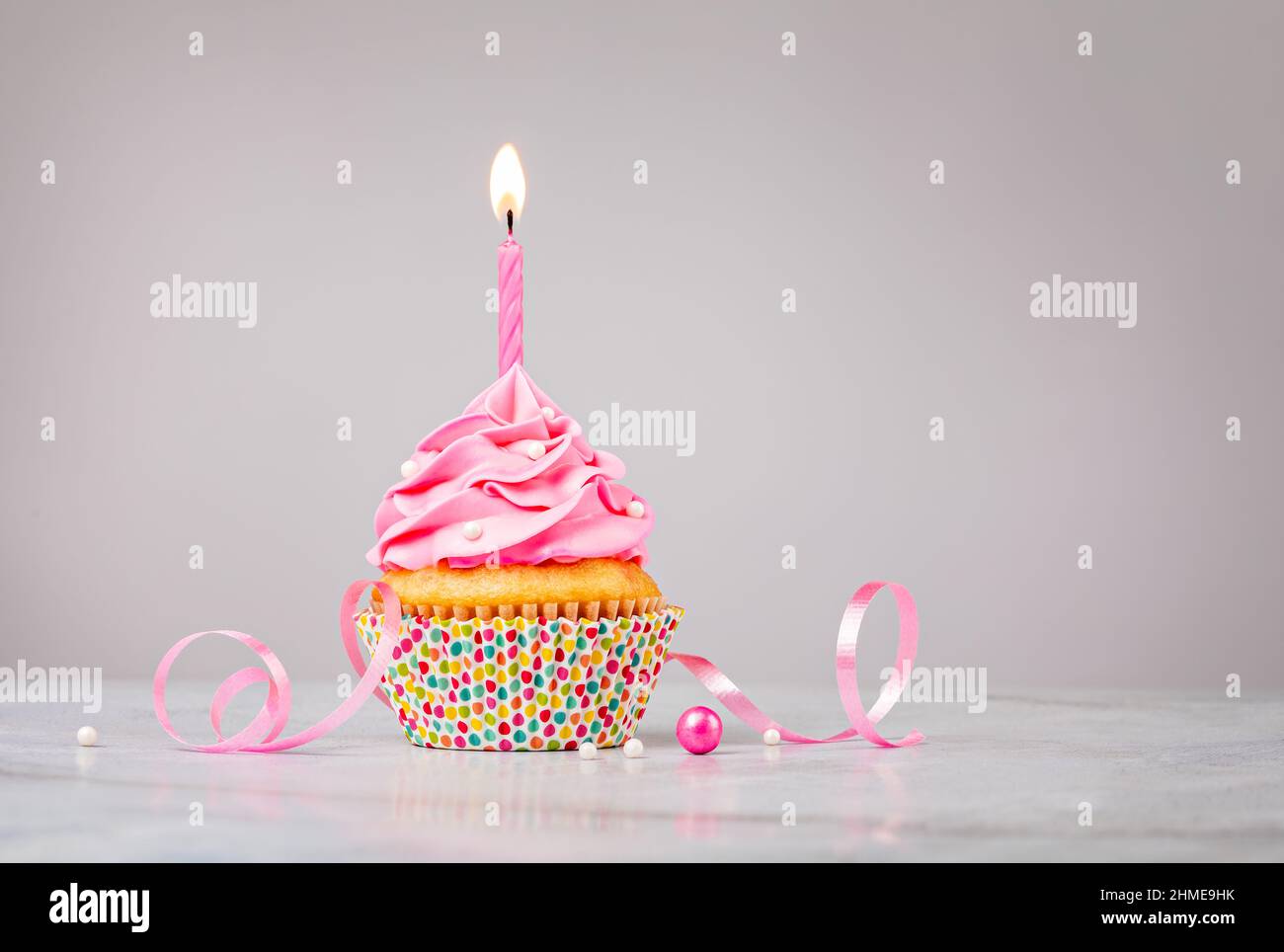 Niedlicher rosa Geburtstagskuchen mit Kerze und bestreut auf hellgrauem Hintergrund. Stockfoto