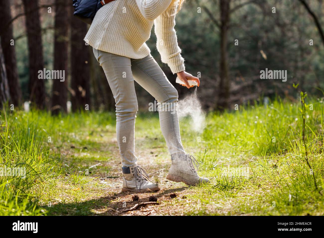 Frau sprüht Insektenschutzmittel gegen Zecke an ihre Beine. Schutz vor Mückenstich während der Wanderung im Wald Stockfoto