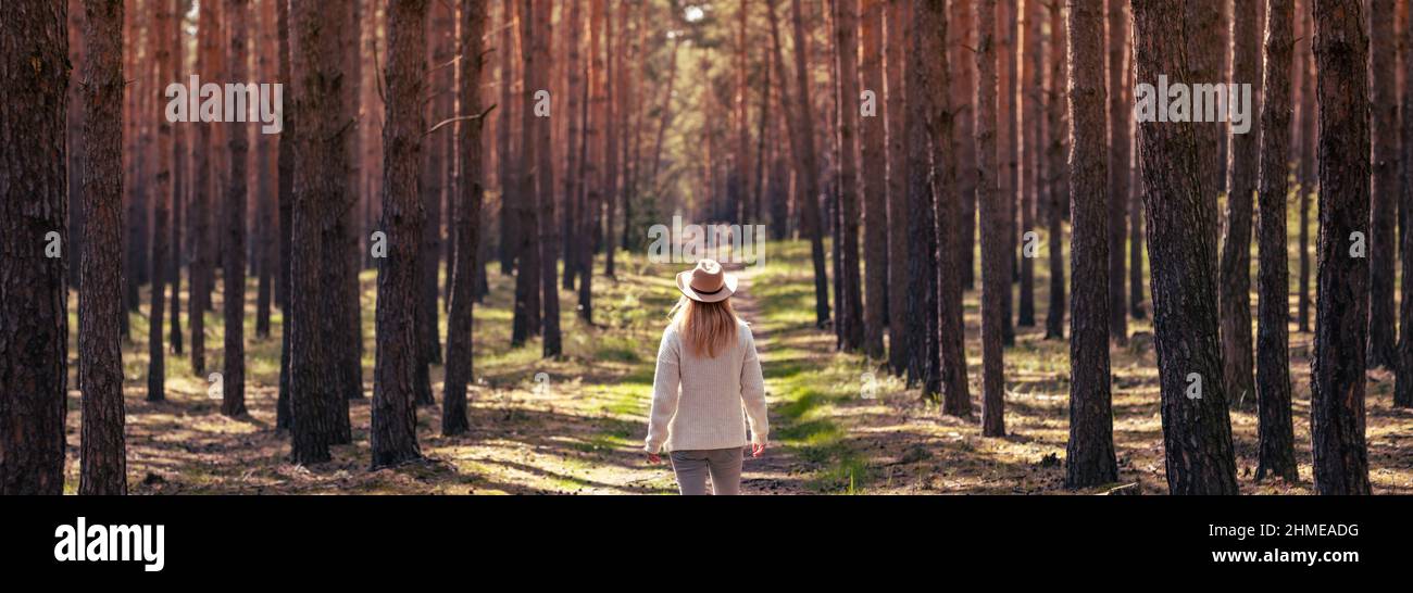 Frau mit Cowboyhut beim Wandern auf dem Wanderweg im Wald. Panoramablick auf den Pinienwald. Wandergenuss in der Frühlingsnatur Stockfoto