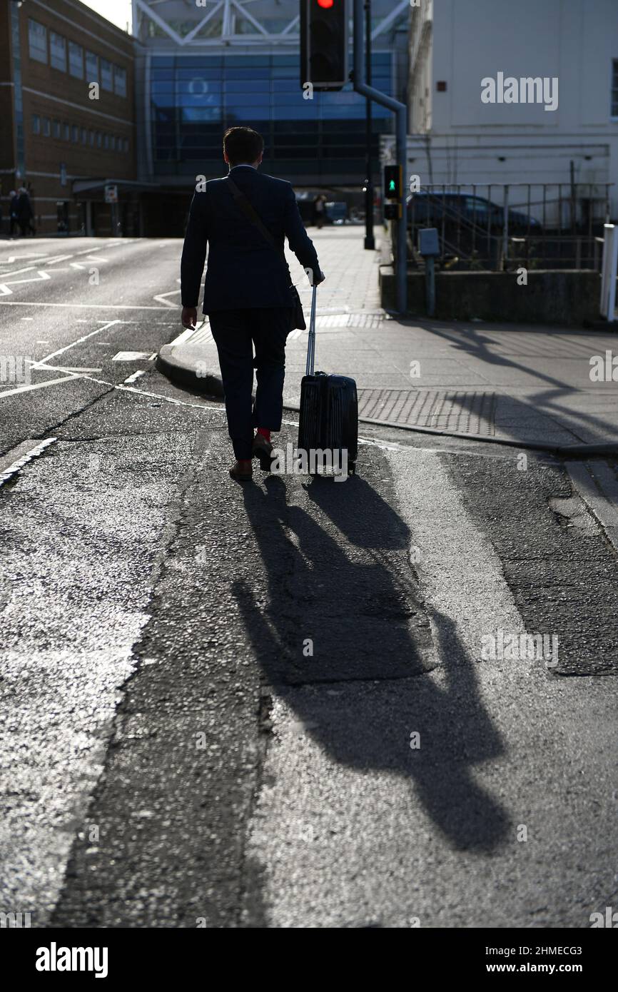 Mögliches Konzeptbild, eine Silhouette eines Mannes in einem Anzug, der mit einem Rollkoffer-Trolley mit einem perfekten Schatten seiner Linie hinter dem Bürgersteig läuft. Stockfoto
