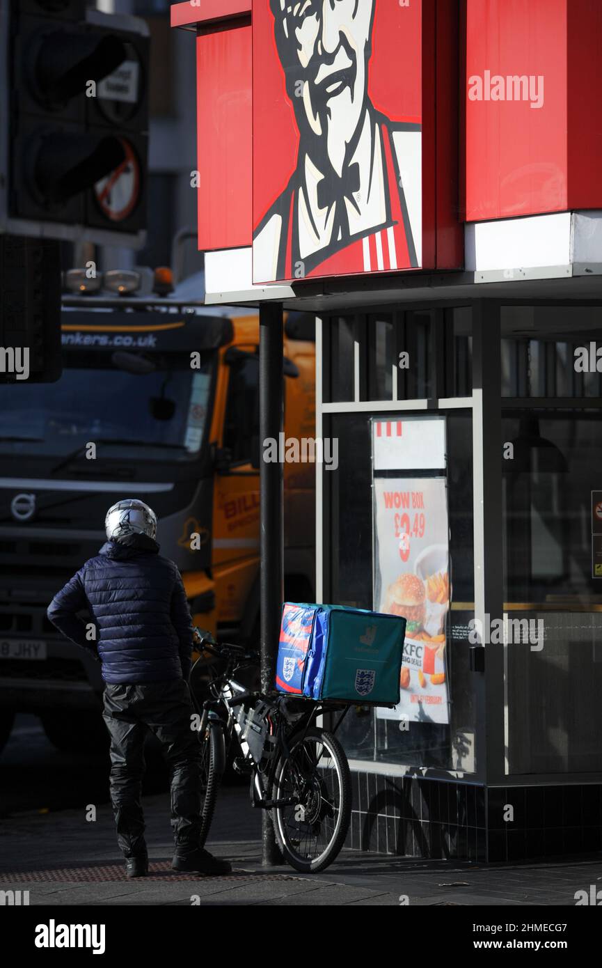 Ein deliveroo Bike Rider wartet vor dem Kentucky Fried Chicken Fast Food Restaurant auf einen Auftrag, der für die Lieferung vorbereitet wird. Stockfoto