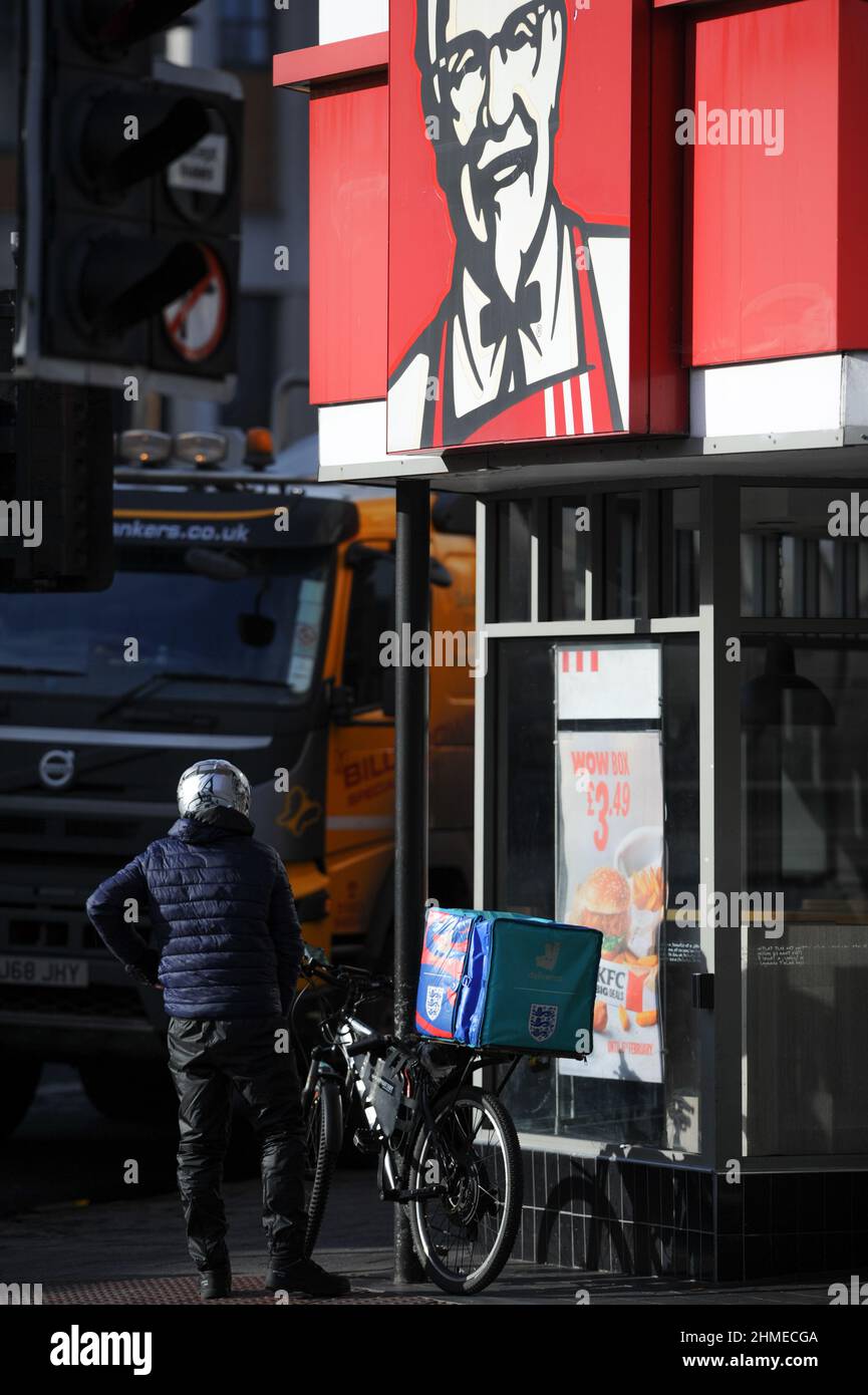 Ein deliveroo Bike Rider wartet vor dem Kentucky Fried Chicken Fast Food Restaurant auf einen Auftrag, der für die Lieferung vorbereitet wird. Stockfoto