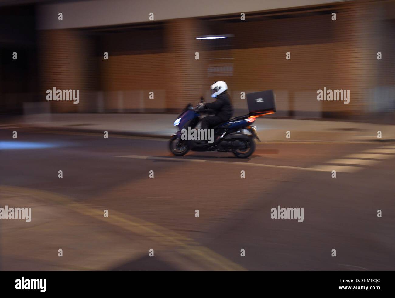 Ein Schwenk mit Bewegung und Kopieplatz eines Motorradfahrers, der nachts mit Lebensmitteln unterwegs ist. Stockfoto