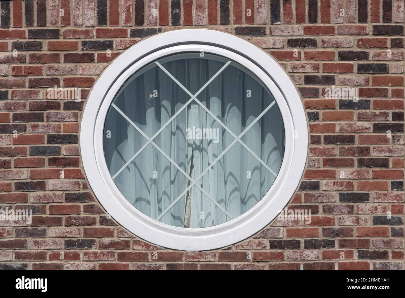 Weiß gerahmtes rundes Fenster in einer roten Ziegelwand Stockfoto