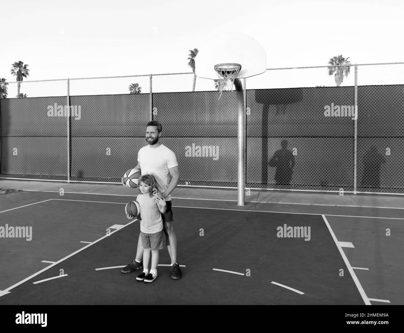 Fröhlicher Vater und Sohn spielen Basketball mit Ball auf dem Spielplatz, glückliches Wochenende Stockfoto