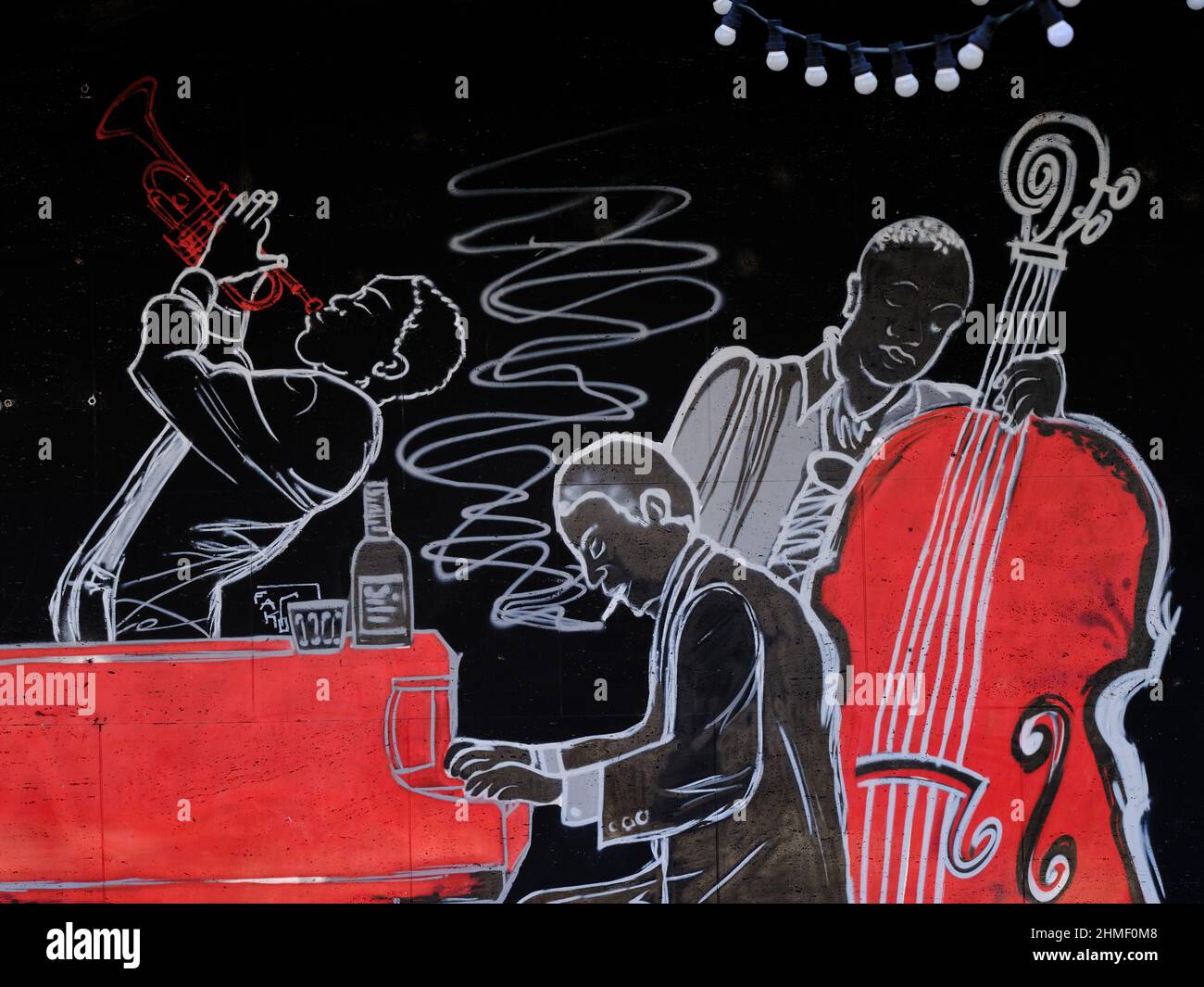 Graffiti an einer Wand mit stilisierten Jazzmusikern mit Trompete, Klavier und Kontrabass in Rot, Schwarz und weiß. Stockfoto