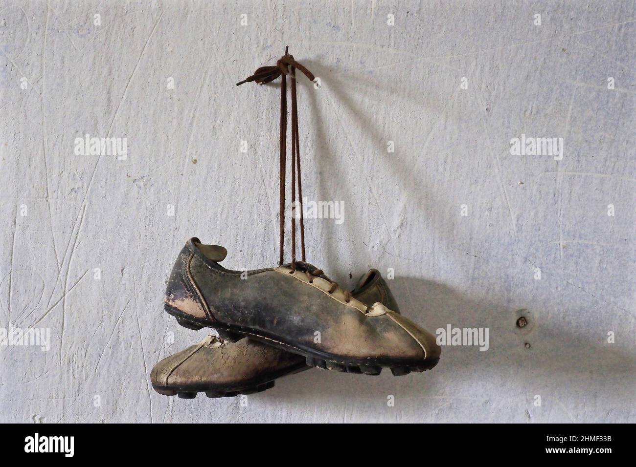 Fußballschuhe, die am Nagel hängen, Sportschuhe für Herren, heruntergekommener Lederschuh, verfaulter Schuh, Schuhwrack, Fauler Kicker, abgenutzter Schuh, abgewohnt Stockfoto