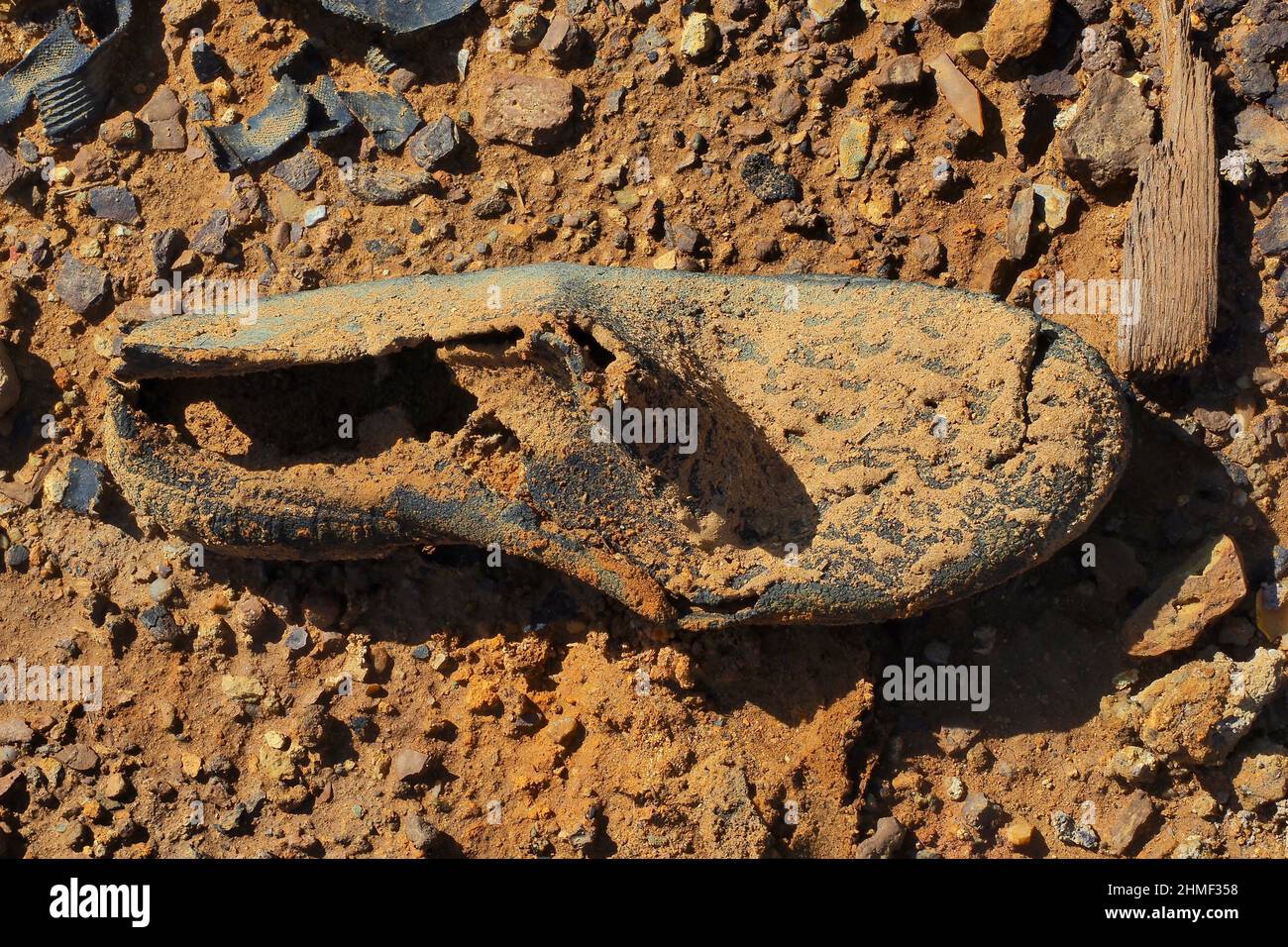 Fragment von Gummistiefel auf roter Erde, verfaulte Schuhe auf dem Boden, verfaulter Schuh, Schuhwrack, verfaulter Kicker, abgenutzter Schuh, Abgenutzter Schuh Stockfoto