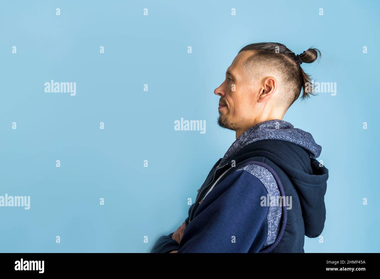 Nahaufnahme eines Seitenprofils Ein Mann mit einer Frisur Top Knot oder Einem Männerbun auf blauem Hintergrund, Männerfrisuren, Haarpflege Stockfoto