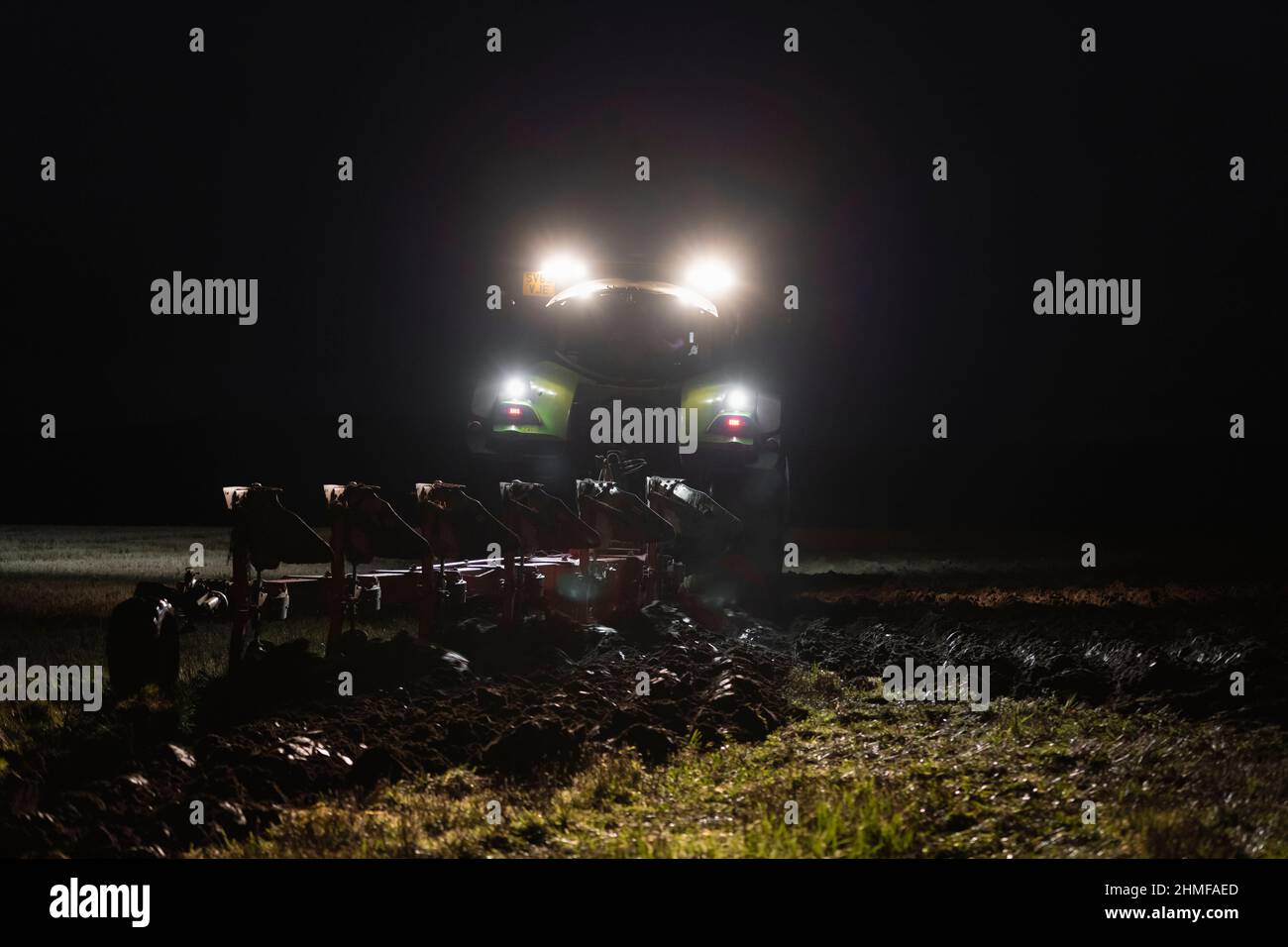 Ein Bauer, der am Abend pflügt, nach Einbruch der Dunkelheit, im Winter auf einer Farm in Schottland durch das Licht der Scheinwerfer des Traktors Stockfoto