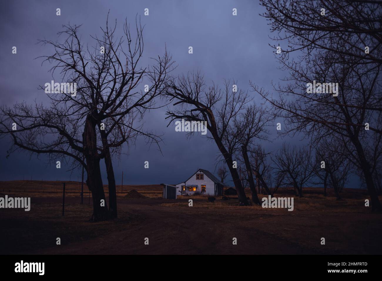 Bauernhaus bei Sonnenaufgang mit Bäumen und unheilvollen Himmel Stockfoto