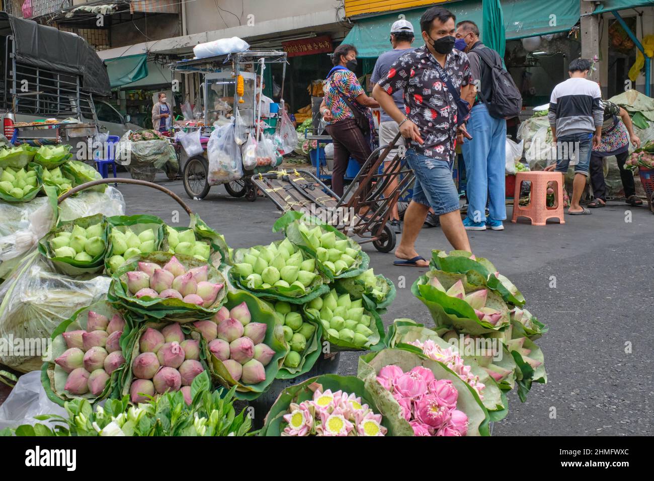 Ein Portier mit seinem Trolley kommt an einem Straßenstand mit Lotusknospen vorbei; am Pak Klong Talat, einem Markt, der für seine große Blumenvielfalt bekannt ist, in Bangkok, Thailand Stockfoto