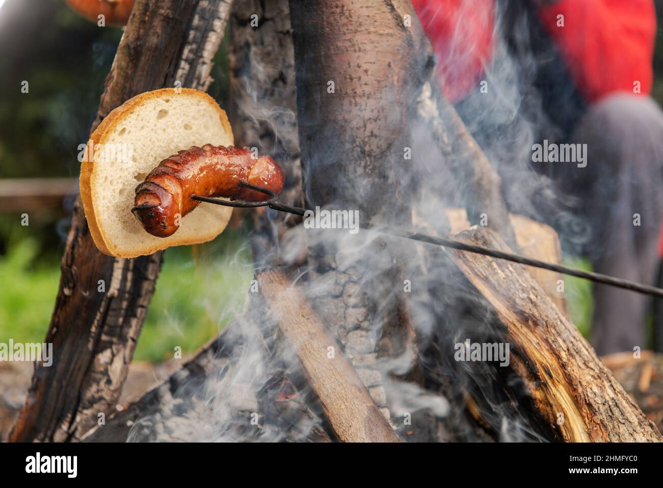 Brennen von polnischer Wurst und einem Stück Weißbrot auf einem Lagerfeuer. Camping Food Thema. Stockfoto