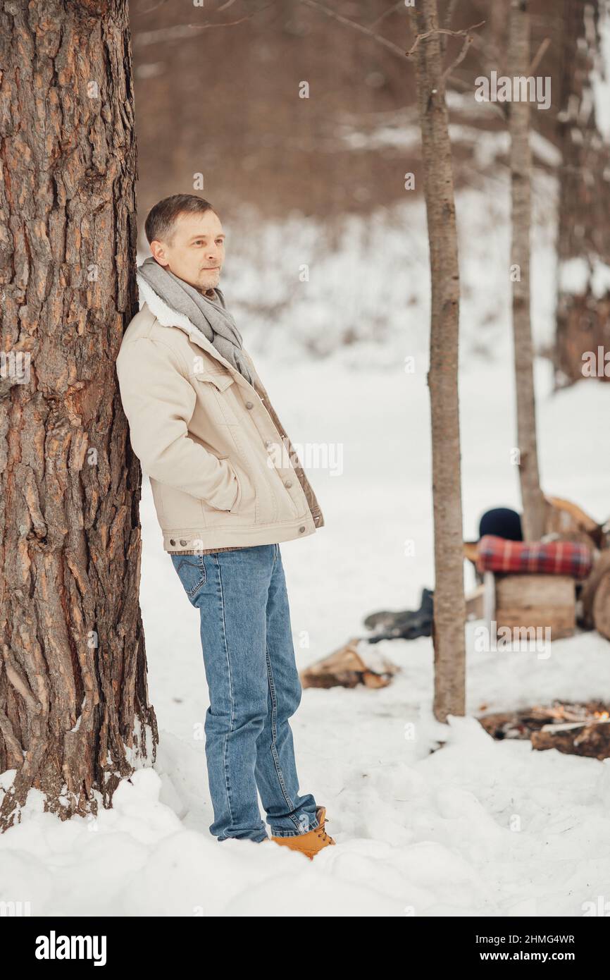 Ein brutaler Mann im Winterwald am Feuer, der Kaffee trinkt Stockfoto