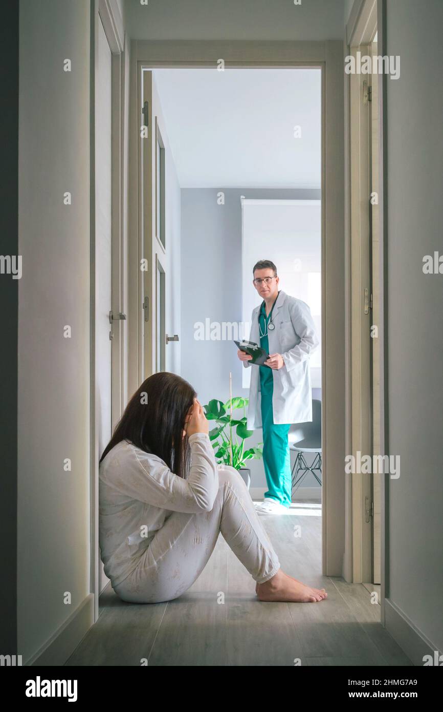 Ärztin, die eine Patientin mit psychischen Störungen auf dem Boden im Flur des Zentrums für psychische Gesundheit ansieht Stockfoto