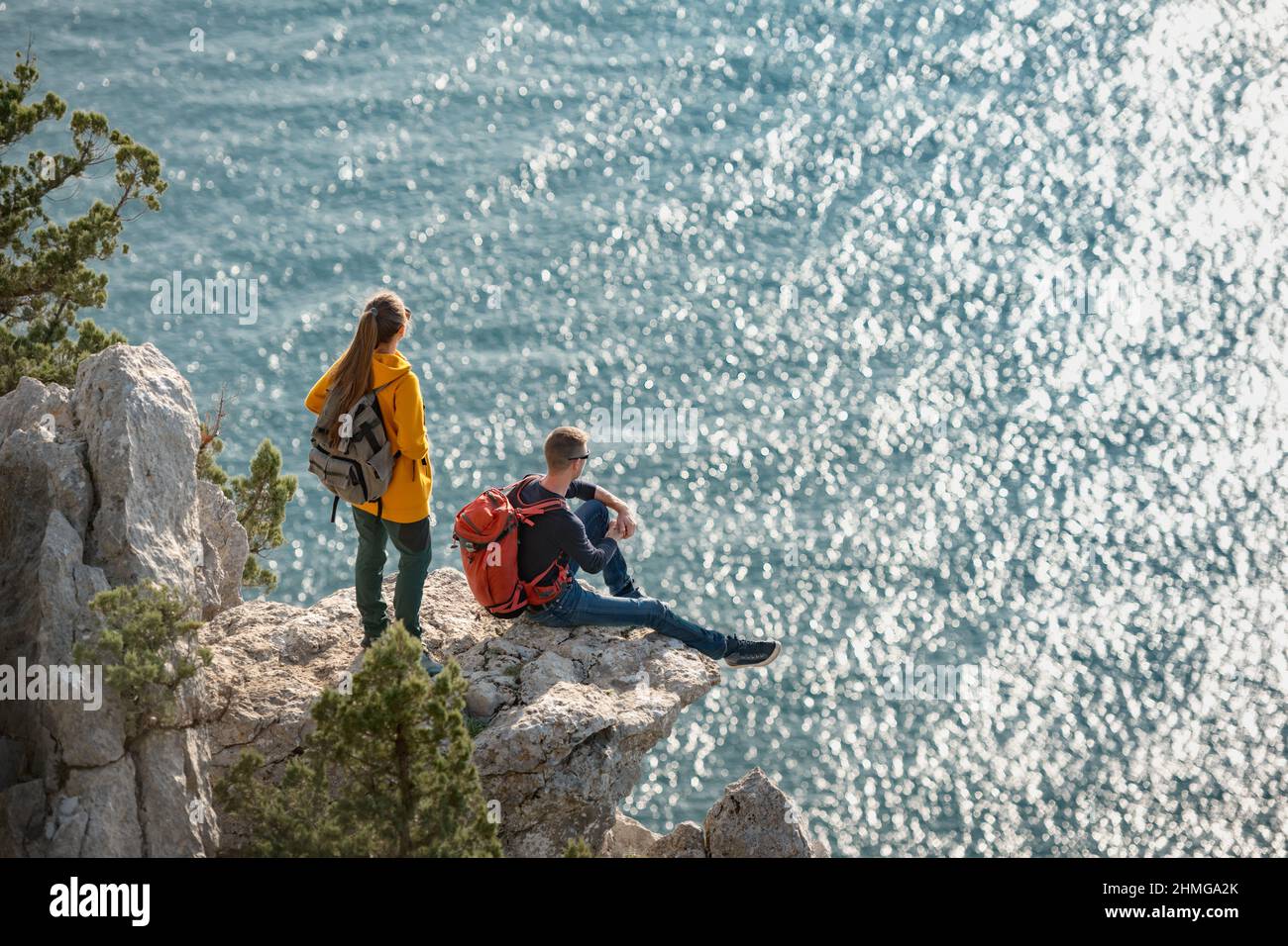 Ein paar Reisende entspannen sich auf einem großen Felsen und blicken auf das Meer Stockfoto