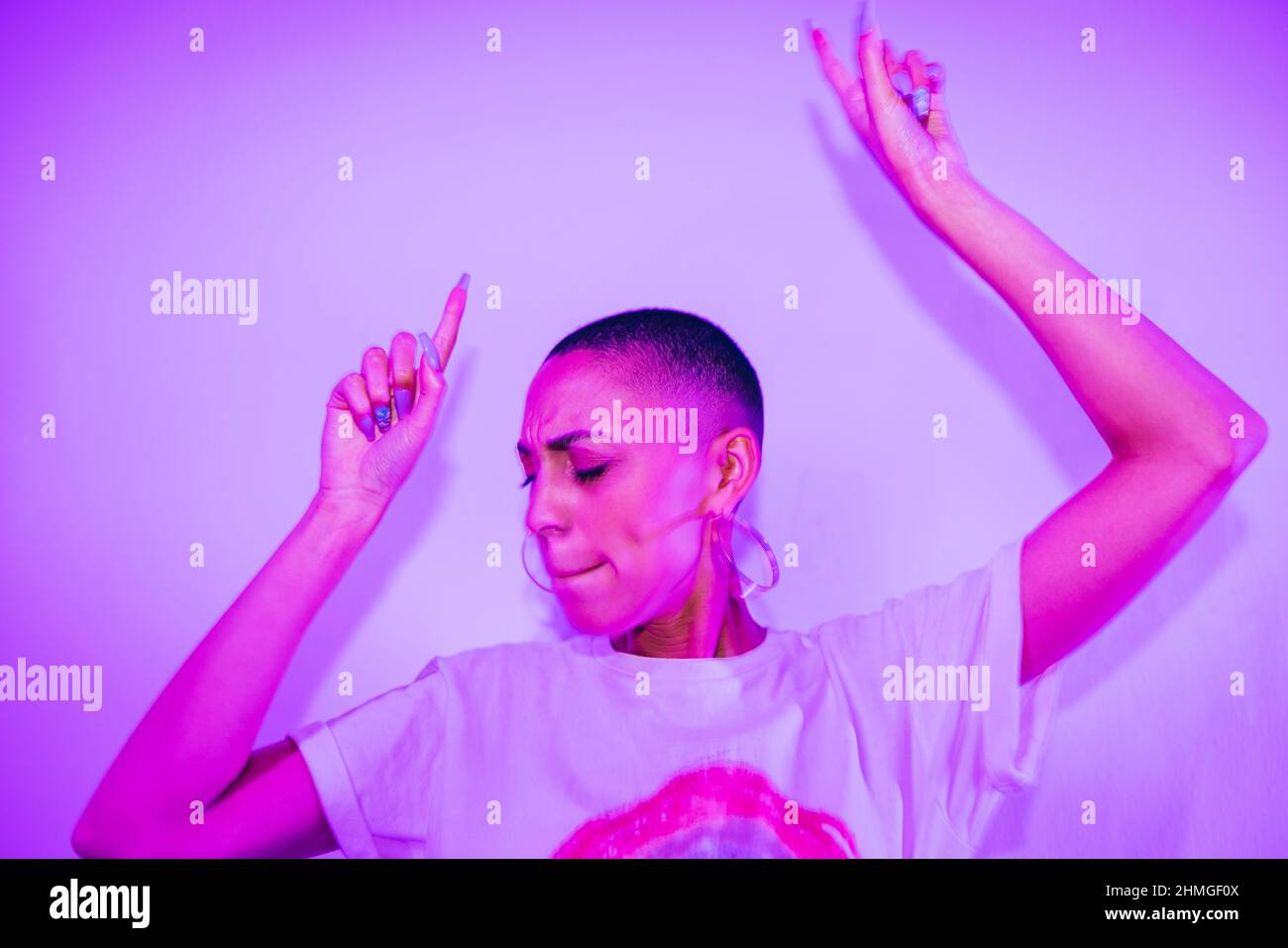 Hipster-Frau, die auf einer Hausparty zu ihrem Lieblingslied tanzt. Lebendige junge Frau, die allein in hellem Neonlicht steht. Junge Frau mit Spaß ein Stockfoto