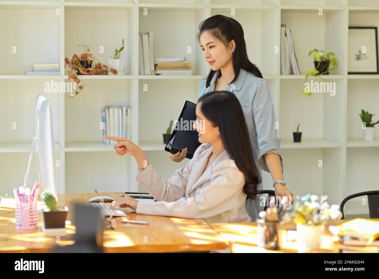 Eine erfolgreiche und professionelle asiatische Managerin, die im Büro die Arbeit ihrer Assistentin auf dem pc-Desktop-Bildschirm überprüft. Geschäftsfrauen concep Stockfoto