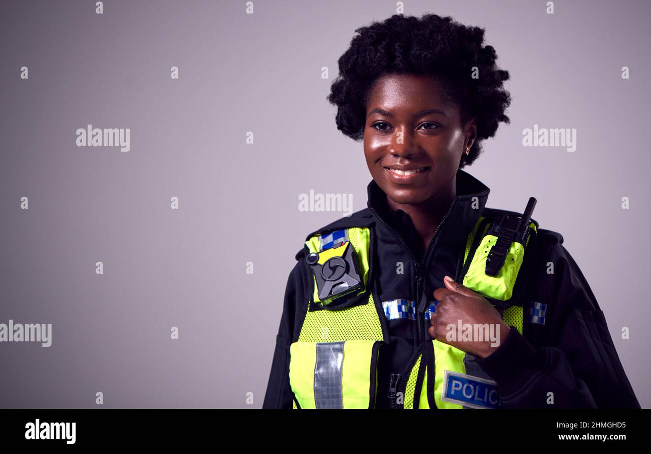 Studio Portrait Of Smiling Young Female Police Officer Against Plain Background Stockfoto