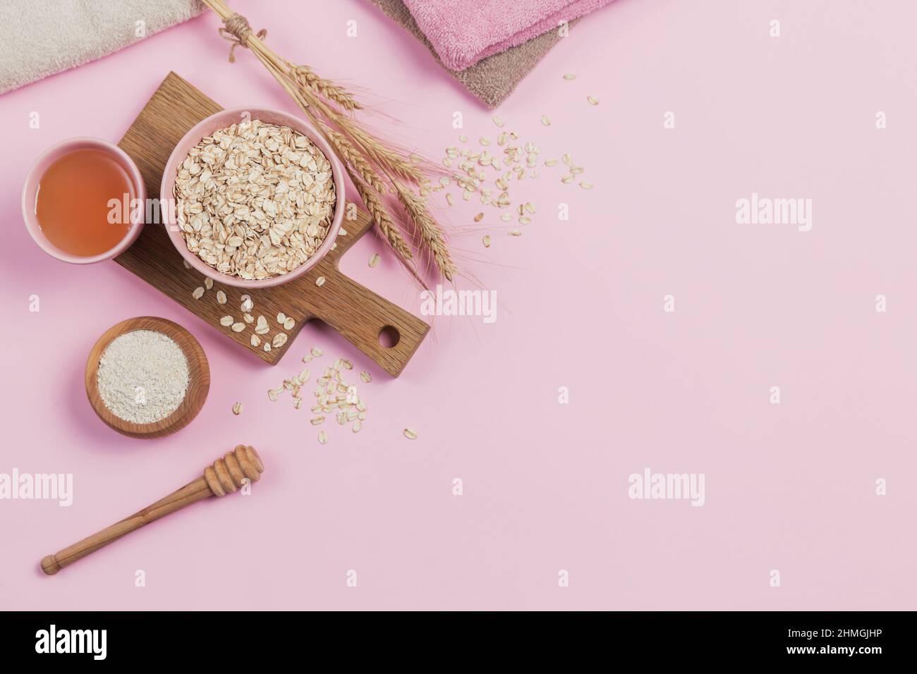 Zutaten für die Herstellung von hausgemachten Gesichtsmaske oder Peeling. Schüssel mit trockenen Haferflocken mit Honig, Haferflocken und Ähren aus Weizen Stockfoto