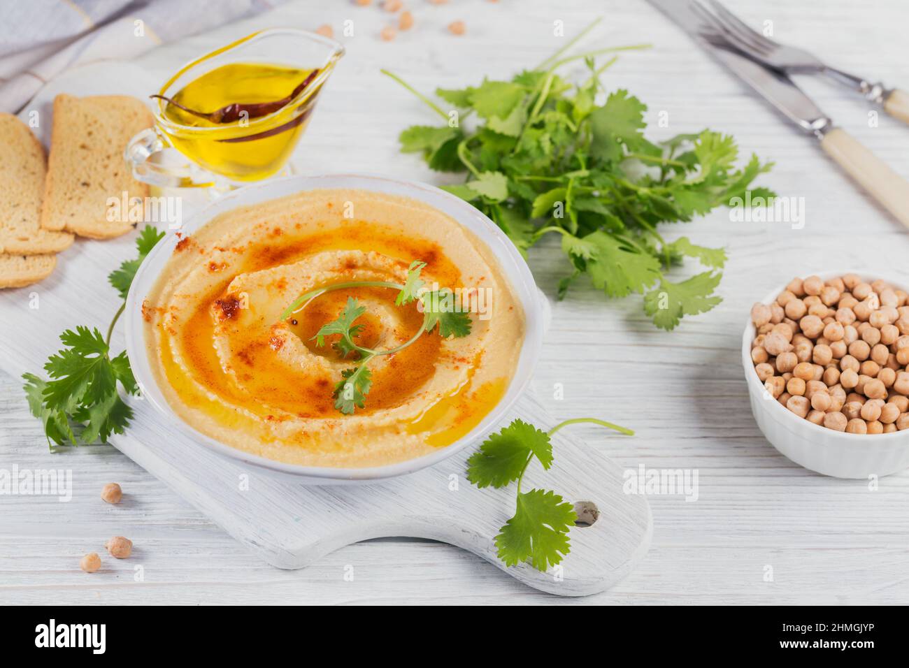 Eine Schüssel mit Kichererbsen hausgemachten Hummus mit Olivenöl, Koriander und geräuchertem Paprika auf weißem Holzhintergrund. Stockfoto